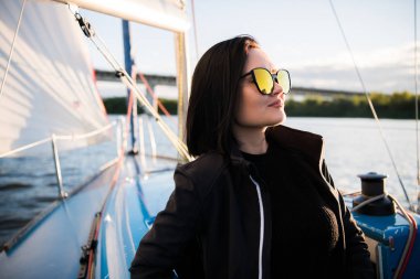 Genç gülümseyen esmer kadın güneşli bir sonbahar günde tekne bir gemide otururken, bir deniz veya nehir üzerinde yürürken güneş gözlüğü takıyor