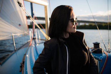 Güzel esmer kız bir gökyüzü arka plan ve okyanus üzerinde siyah ceket. Yat ve tekne seyahat