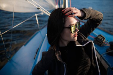 Genç gülümseyen esmer kadın güneşli bir sonbahar günde tekne bir gemide otururken, bir deniz veya nehir üzerinde yürürken güneş gözlüğü takıyor