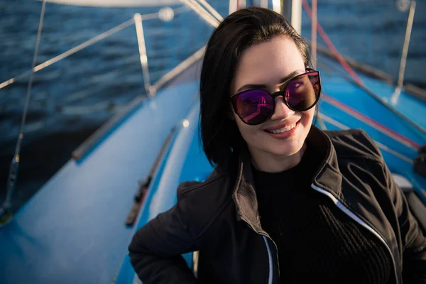 Hermosa chica morena en una chaqueta negra sobre un fondo del cielo y el océano. Viajar en barco o yate — Foto de Stock