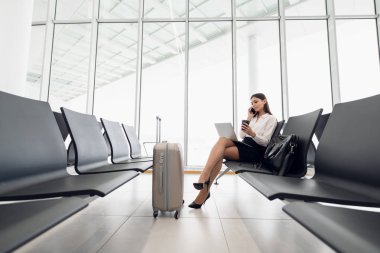 Akıllı telefonuyla havaalanında bekleyen bir iş kadını.