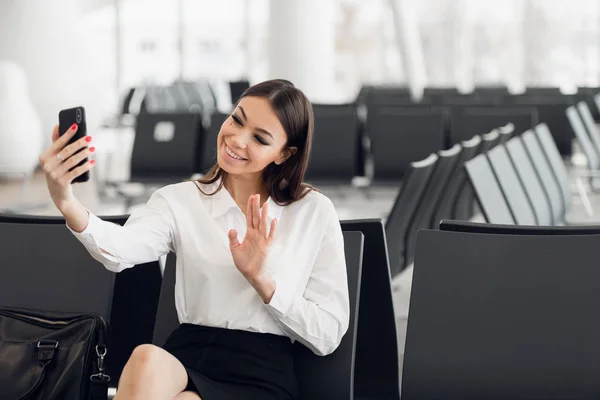 Επιχειρηματίας ταξιδιώτης με smartphone, κουνώντας το χέρι για χαιρετισμό στην μπροστινή κάμερα κατά τη διάρκεια βιντεοκλήσης, περιμένοντας στην αίθουσα αναμονής στο αεροδρόμιο. Γυναίκα επιβάτης που ταξιδεύει στο εξωτερικό για επαγγελματικό ταξίδι. Αεροπορική πτήση — Φωτογραφία Αρχείου