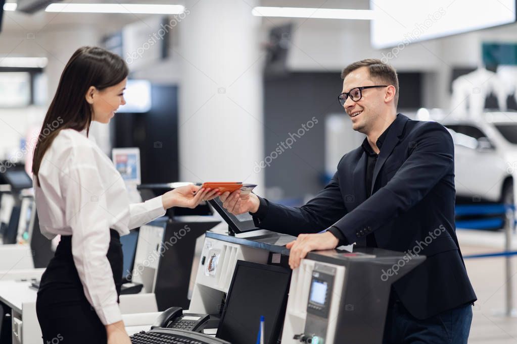 Business trip. Handsome young businessman in suit holding his passport and talking to woman at airline check in counter in the airport