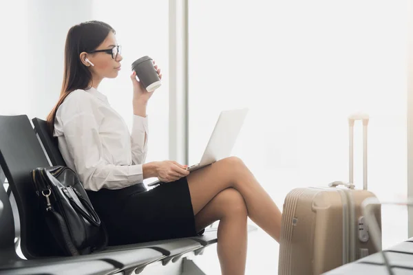 Joven mujer de negocios en el aeropuerto, utilizando el ordenador portátil y beber café, viajes, viaje de negocios y el concepto de estilo de vida activo —  Fotos de Stock