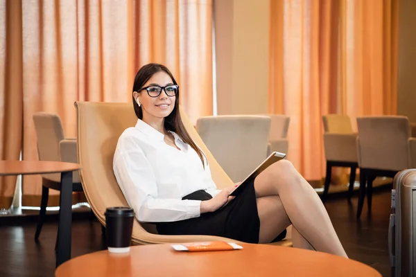 Confident businesswoman listening music on her tablet computer while sitting in chair in airport business lounge