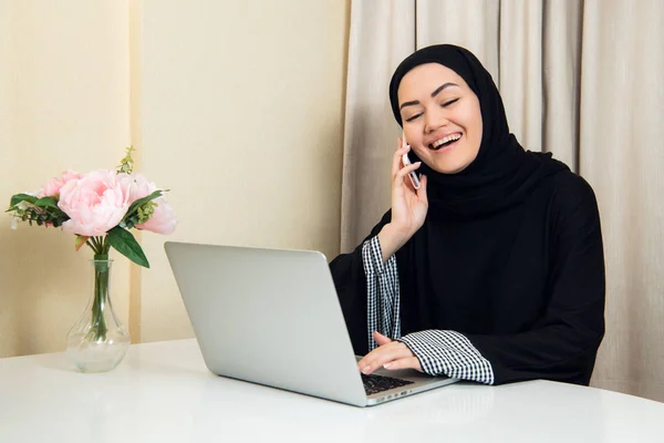 Trabajadora musulmana hablando por teléfono mientras trabaja con computadora portátil — Foto de Stock