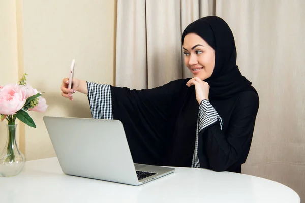 Chica muy bonita en hijab negro tomando una selfie increíble con su teléfono en el trabajo o en casa . — Foto de Stock