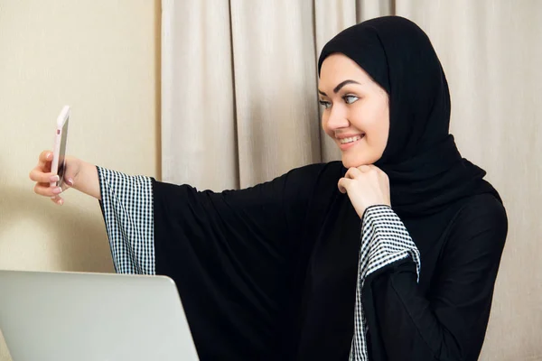 Chica muy bonita en hijab negro tomando una selfie increíble con su teléfono en el trabajo o en casa . — Foto de Stock