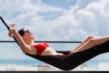 Lüks bir otelin çatısındaki havuzda hamakta dinlenen güzel bir kız. Mavi bir okyanusa ve gökyüzüne bak.