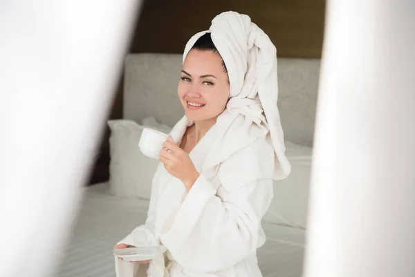 Una chica en un albornoz bebiendo café por la mañana en el alféizar de la ventana . —  Fotos de Stock