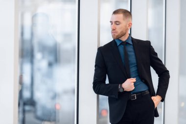 Pencerenin yanında elleri çapraz olan kendine güvenen bir iş adamının portresi..