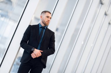 Pencerenin yanında elleri çapraz olan kendine güvenen bir iş adamının portresi..