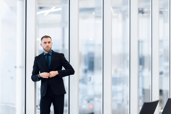 Stilvoller junger Geschäftsmann im modernen Anzug, der ein Leistungsträger ist, steht in der obersten Etage eines Bürogebäudes und blickt durch große Fenster auf die Aussicht — Stockfoto
