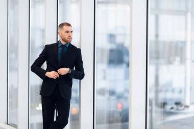Cam kapının önünde takım elbiseli ve kravatlı yakışıklı bir adamın portresi.
