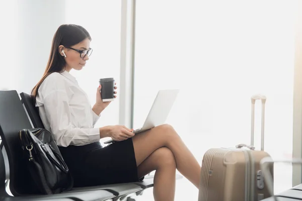 Mujer joven con café trabajando en el ordenador portátil sentado en una sala de salida del aeropuerto —  Fotos de Stock