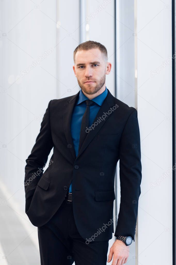 Portrait of handsome man standing in a suit and tie in front of glass door