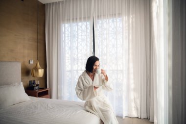 Sabahları hafif bir odada yatakta kahve içen bornozla bir kız..