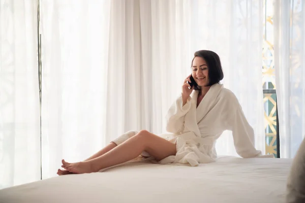 Mujer usando tableta en una cama de hotel usando albornoz — Foto de Stock