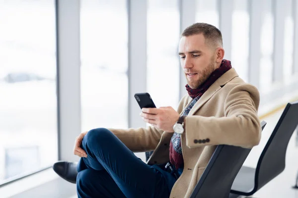 Joven hombre ocupado esperando la salida en el aeropuerto mientras usa su teléfono —  Fotos de Stock