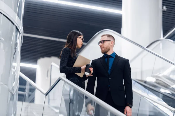 Piękna kobieta biznesu i mężczyzna ich trzymając tablet w rękach i rozmawiając ze sobą stojąc na schodach w nowoczesnym budynku biurowym. — Zdjęcie stockowe