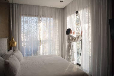 Beyaz bornoz giyen kadın ışık odasında pencereyakınında sabah ayakta