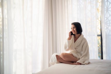 Bornoz giyen bir otel odasında ki yatakta tablet kullanan kadın