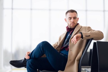 Genç iş adamı havaalanında bekliyor. Saati kontrol ediyor..