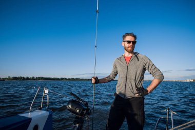 Yat Kaptan sakallı bir yelkenli yatta yelken boom duruyor ipi elinde tutan ve gülümseyerek, mutlu hissediyor. Yetişkin yachtsman dünya çapında seyahat. Kopya alanı