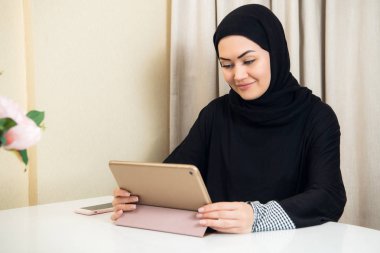 Kulaklık giyen Müslüman kadın evde tablet bilgisayar ile oturup. Evde, bir film izlemek ya da bir müzik dinlemek hazırlanıyor dinlenme.