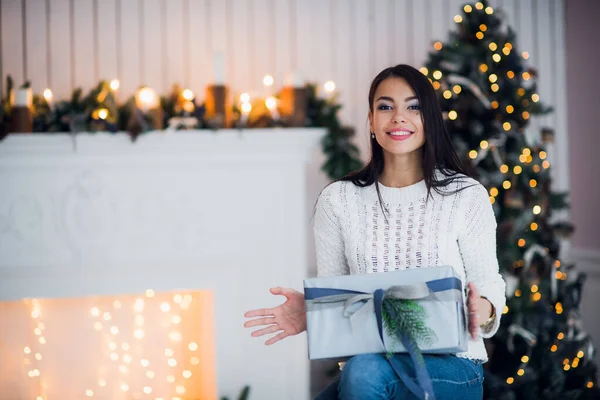 Fiatal nő portré tartja ajándék. Mosolygó boldog lány előtt karácsonyfa és díszített kandalló. — Stock Fotó
