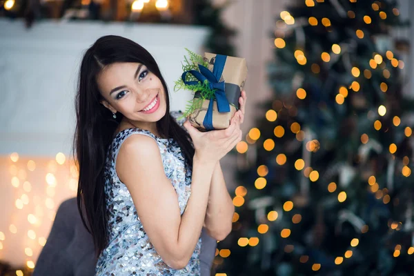 若い女性の肖像は贈り物を保持します。クリスマスツリーと装飾された暖炉の前で笑顔幸せな女の子. — ストック写真