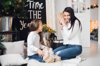 Mutlu Noeller ve mutlu tatiller. Neşeli anne ve tatlı kızı Noel hediyesini açıyorlar. Ebeveynler ve küçük çocuklar Noel ağacının yanında eğleniyorlar.