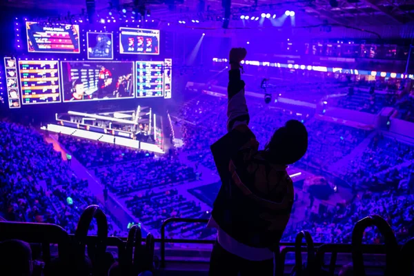 Big esports event. Video games fan on a tribune at tournaments arena with hands raised. Cheering for his favorite team.