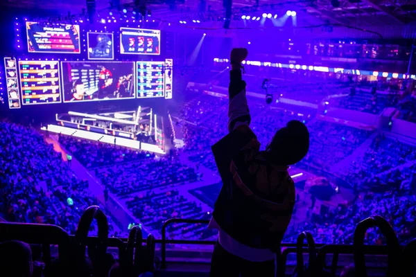 Büyük Esport etkinliği. Turnuva arenasında bir tribünde elleri havada bilgisayar oyunları hayranı. En sevdiği takım için tezahürat yapıyor..