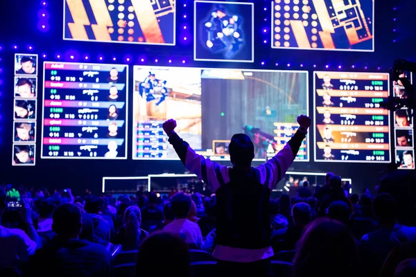 MOSCÚ, RUSIA - 14 DE SEPTIEMBRE DE 2019: evento de videojuegos de esports. Feliz fanático dedicado a los deportes electrónicos animando a su equipo favorito en una tribuna frente a una pantalla grande con la mano levantada . —  Fotos de Stock