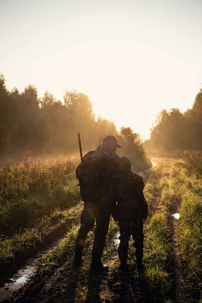 Rifle Hunter και ο γιος του Silhouetted στο όμορφο ηλιοβασίλεμα. Κυνηγός με ένα αγόρι και τουφέκι σε ένα δάσος με την ανατολή του ηλίου. — Φωτογραφία Αρχείου