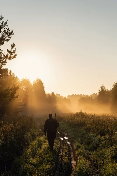 Vintage Hunter camina por el camino del bosque. Rifle Hunter Silhouetted en Beautiful Sunset o Sunrise. Cazador apuntando rifle en bosque — Foto de Stock