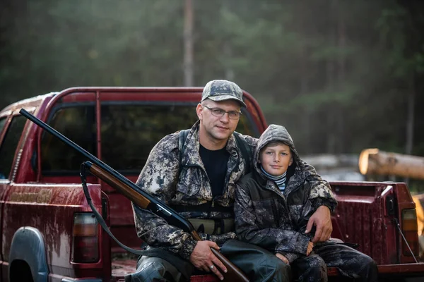 Father and son sitting in a pickup truck after hunting in forest. Dad showing boy mechanism of a shotgun rifle.