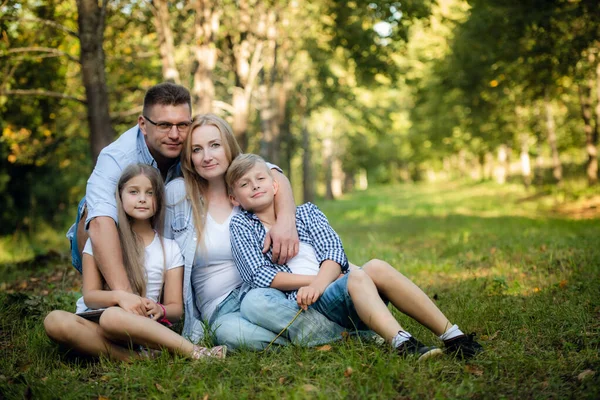 Happy family of four sitting on a grass in summer park outdoors and smiling — Stock Photo, Image