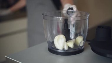 Mutfak ünitesi kullanan bir kadın. İçine soğan koyuyor.