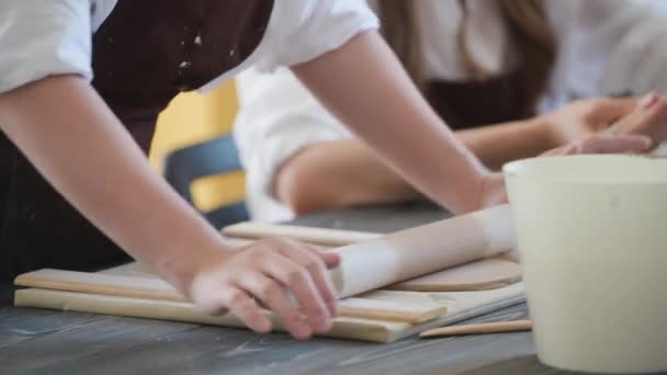 Onherkenbare vrouwelijke handen plat stuk klei liggend op stof met behulp van houten deegroller in keramische studio. — Stockvideo