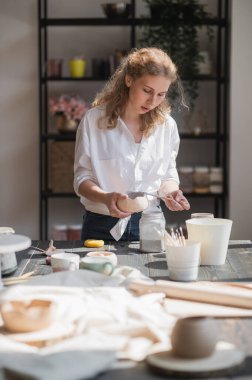 Dişi çömlekçi fırça kullanarak çiğ seramik bardak parlatıyor. Çömlek atölyesine rengarenk koyan çömlek kupası.