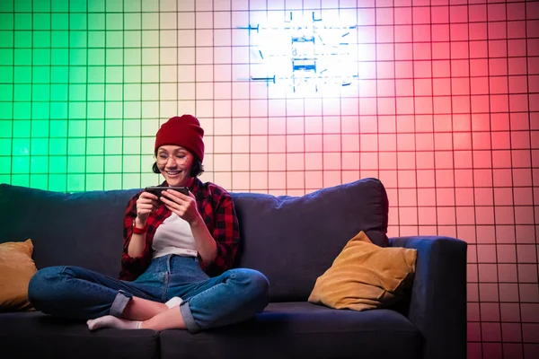 Πορτρέτο νεαρός έφηβος hipster κορίτσι χρησιμοποιώντας έξυπνο κινητό τηλέφωνο στον καναπέ με μαξιλάρια στο εσωτερικό του σαλονιού — Φωτογραφία Αρχείου