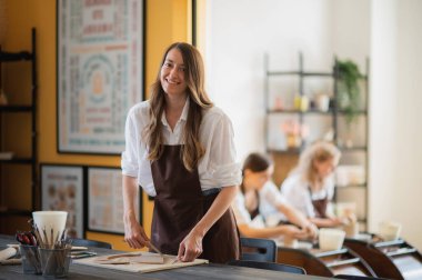 Çömlek kursunda oklavayla çalışan genç bir kadın. Sanatçı, farklı çömlek araçları ile büyük ahşap merdane kullanarak çiğ kil yuvarlar.