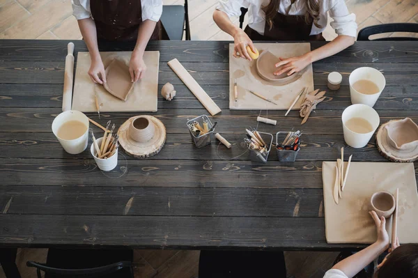 Κάτοψη των γυναικών αγγειοπλαστών κατά τη διάρκεια της εργασίας στο πήλινο εργαστήριο. Οι γυναίκες πλοίαρχοι προετοιμάσει κεραμικά και πήλινα προϊόντα σε μεγάλο ξύλινο τραπέζι — Φωτογραφία Αρχείου