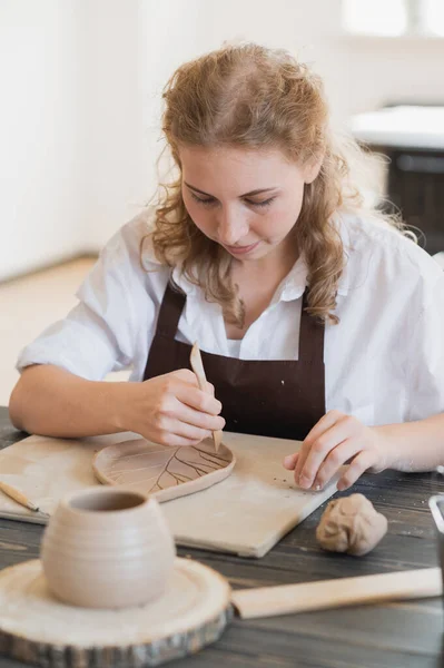 Main féminine tenant le bâton et faisant ornement sur le produit décoratif. Argile maître moulage argile sur un atelier de poterie et de céramique. — Photo