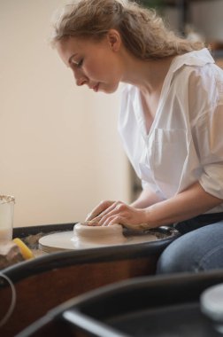 Çömlek çarkında çalışan ve kilden tencere yapan kadın elleri yakından görülüyor. Eller kilden bir kap yontuyor. Çömlekçi çarkında modellik üzerine atölye