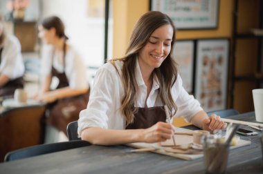 Çömlekçilik sınıfındaki genç bir kadın farklı aletlerle çalışıyor..
