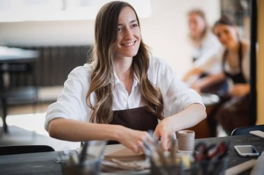 Toprak ürün eğrisi yapan genç bir kadın çömlek atölyesine girdi.