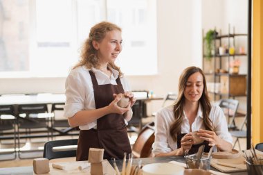 Kadın çömlekçi masadaki kil parçasını şekillendiriyor. Kadın seramik bir şey yapıyor. Sanat stüdyosunda çömlekçilik, el yapımı ve yaratıcı beceriler..